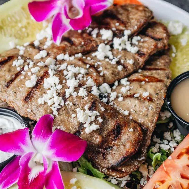Grilled meat with feta, lettuce, cucumber, tomato, sauces, and orchids.