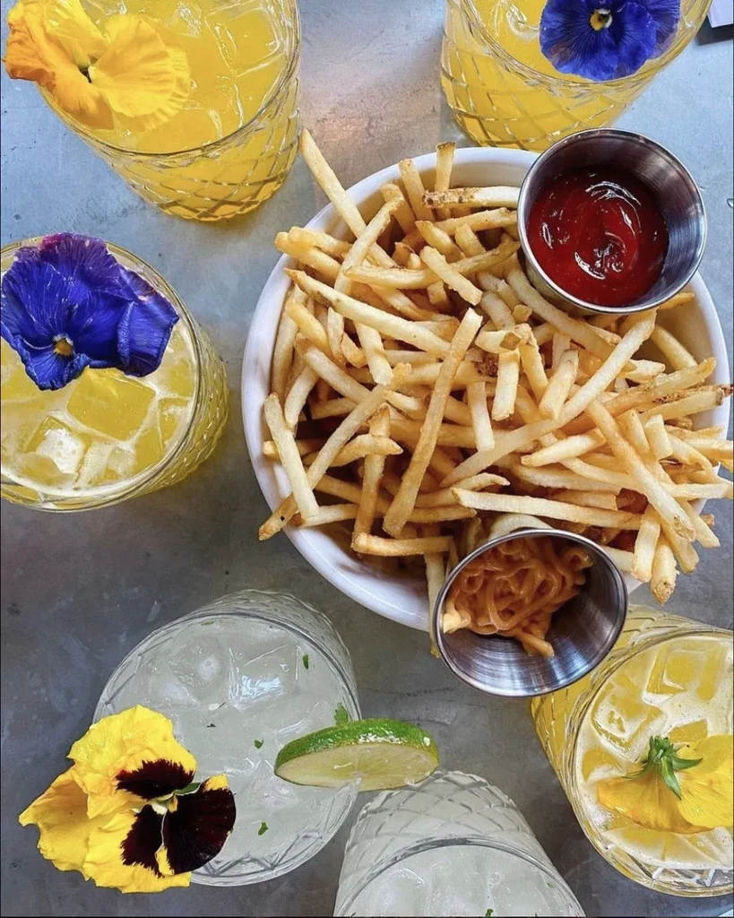 Overhead view of fries, sauces, and pansy-garnished drinks on a table.