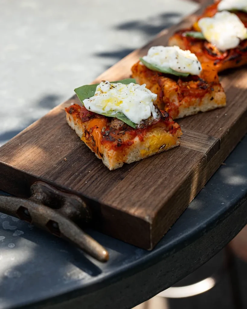 Three rectangular focaccia pieces with burrata, tomato, and basil on a board.