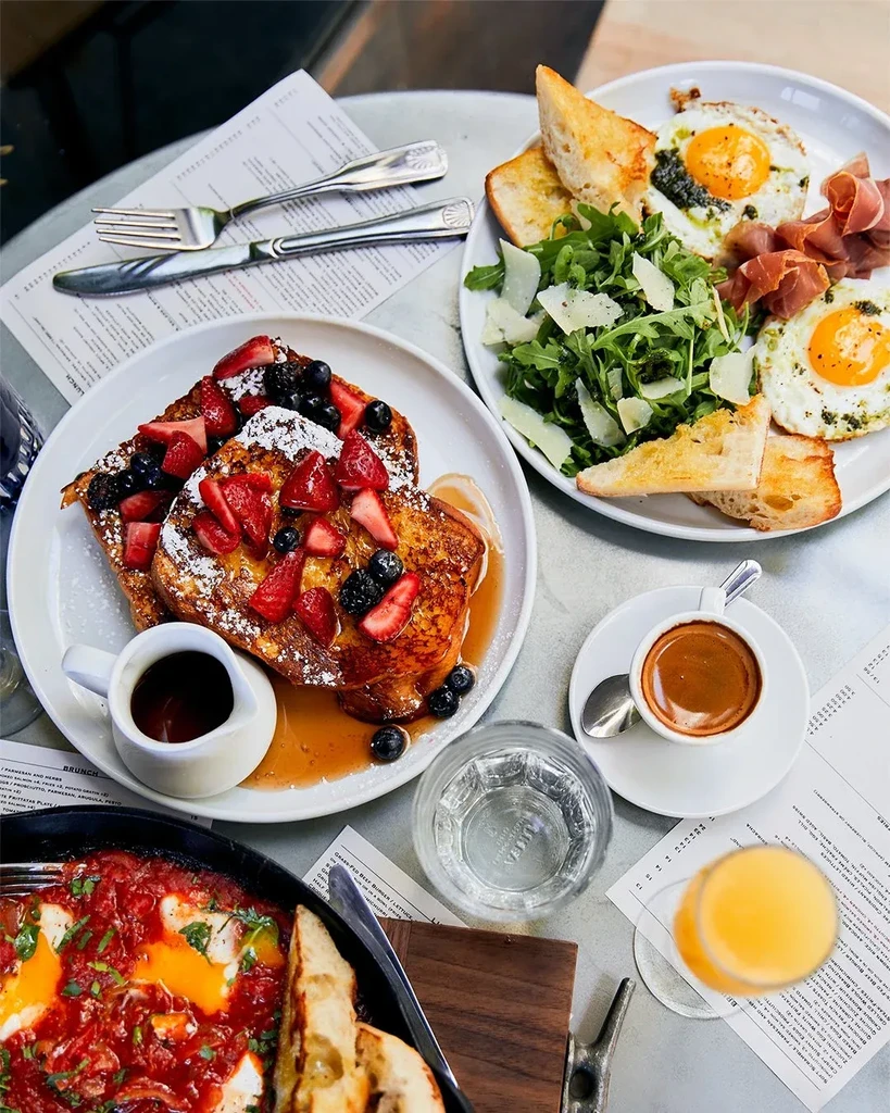 Restaurant brunch flat lay with French toast, shakshuka, fried eggs, and drinks.