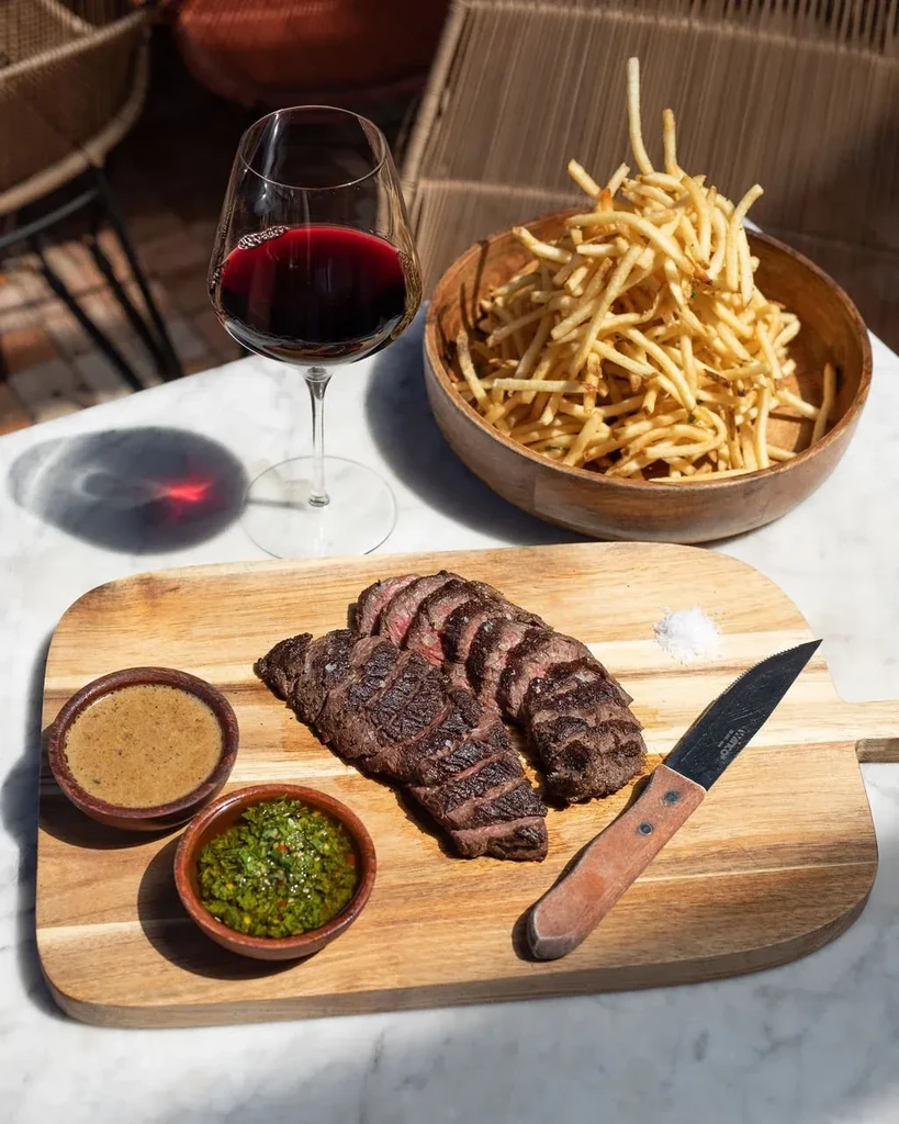 Sliced steak, fries, sauces, and red wine on marble table.