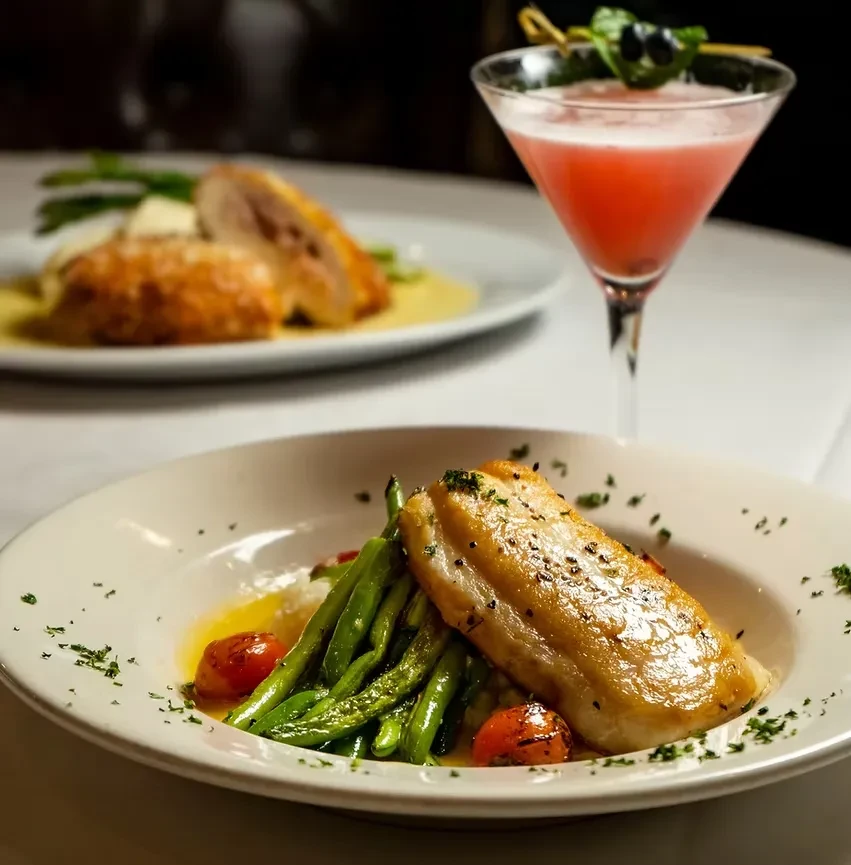 Seared fish, pink cocktail, and chicken dish on a table.