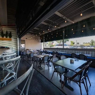 Restaurant patio with wicker seating, string lights, plants, and open view.
