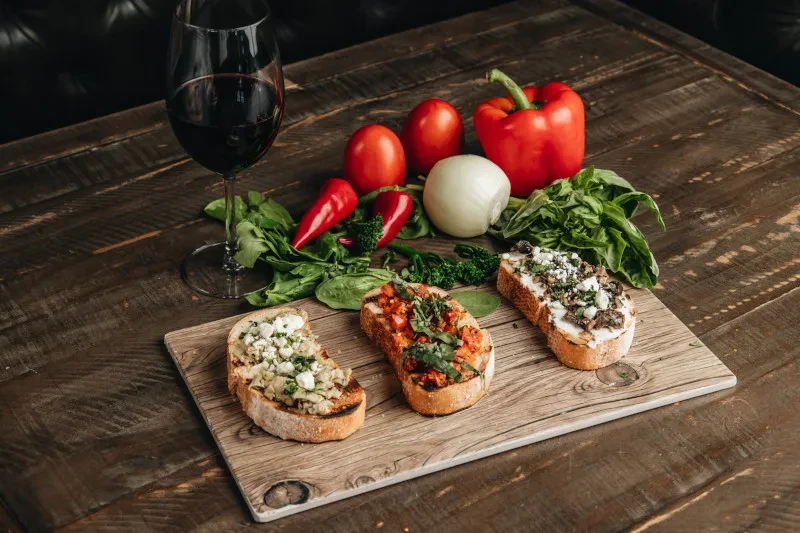 Overhead shot of bruschetta, red wine, vegetables on a rustic table.