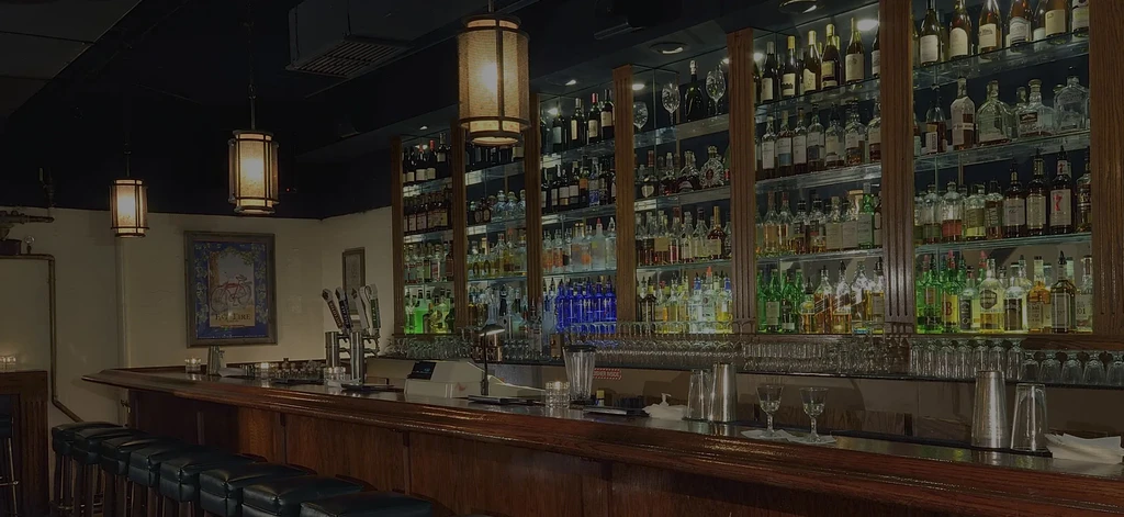 Empty bar with polished dark wood counter and extensive liquor bottles.