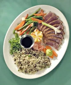 Plated seared tuna with mixed vegetables, wild rice, and sauces.