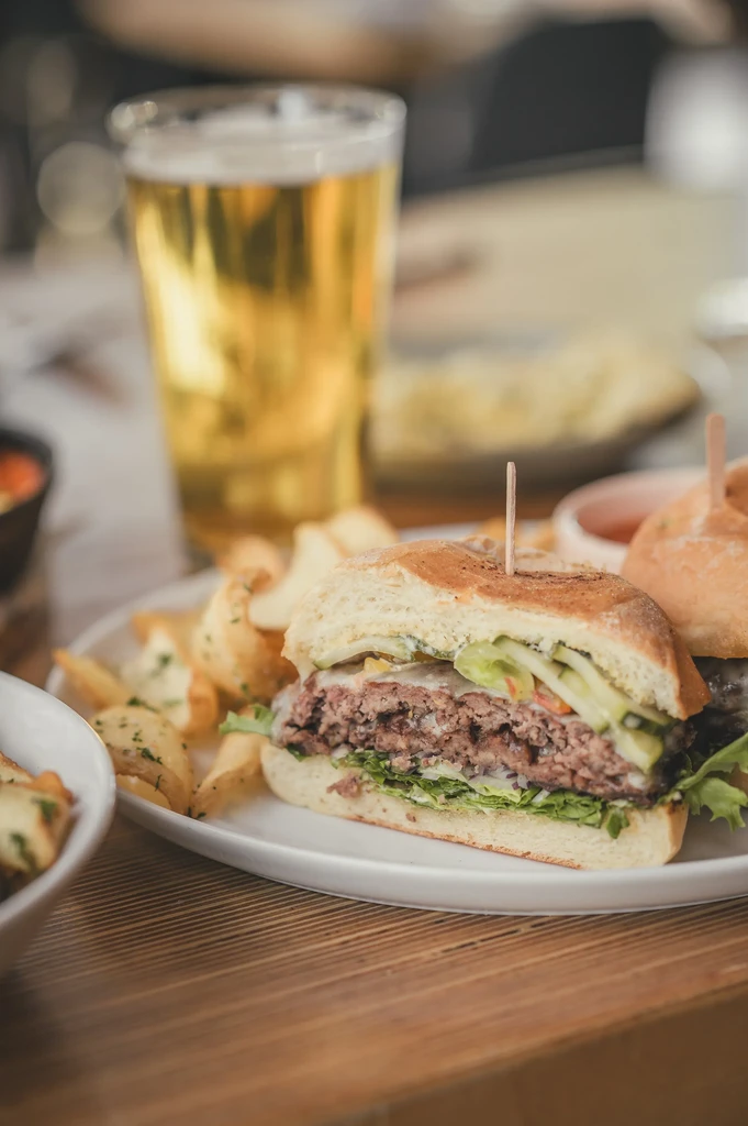 Half-cut burger, potato wedges, and beer on a wooden table.