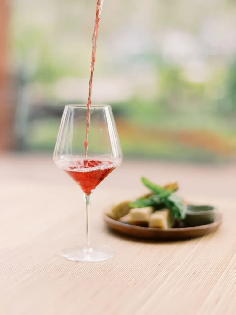 Rosé wine pours into an elegant stemmed glass on a wooden table.