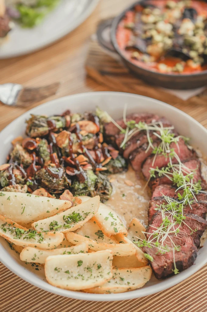 Plate of medium-rare steak, roasted Brussels sprouts, and potato wedges.