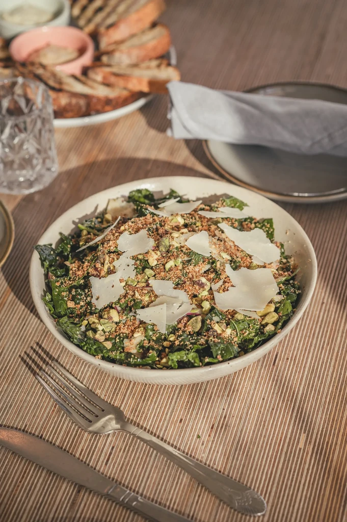 Overhead shot of green salad with pistachios, Parmesan shavings, and breadcrumbs.