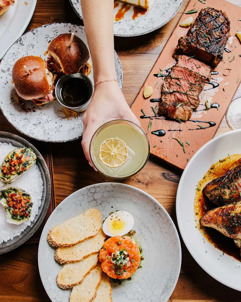 Overhead view: diverse gourmet dishes and a cocktail on a wooden table.