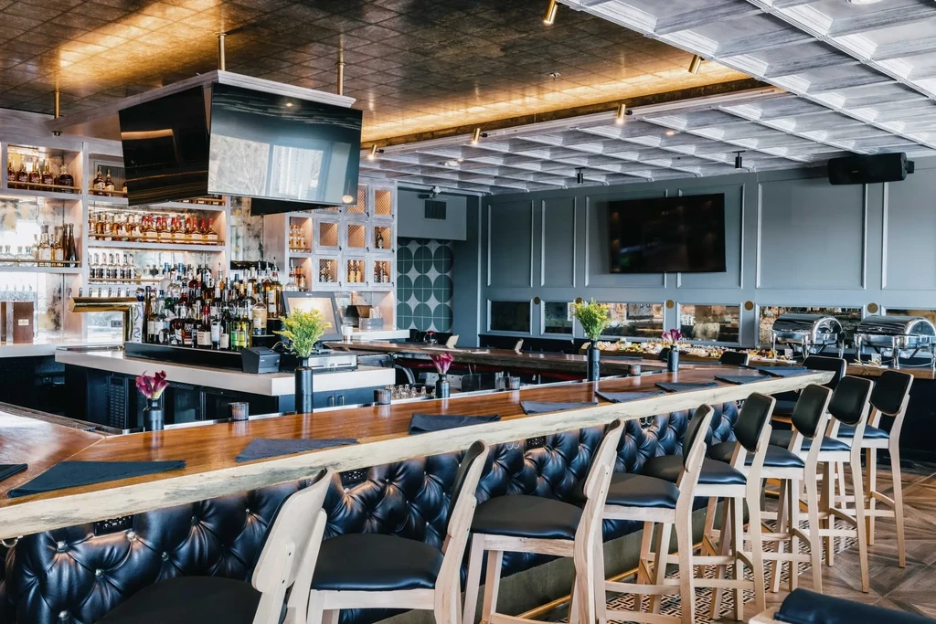Upscale restaurant bar with wooden counter, liquor bottles, TVs, and buffet dishes.
