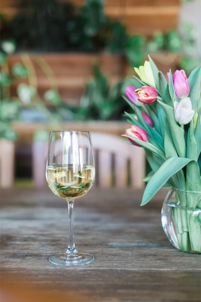 White wine glass and colorful tulips on a rustic wooden table.