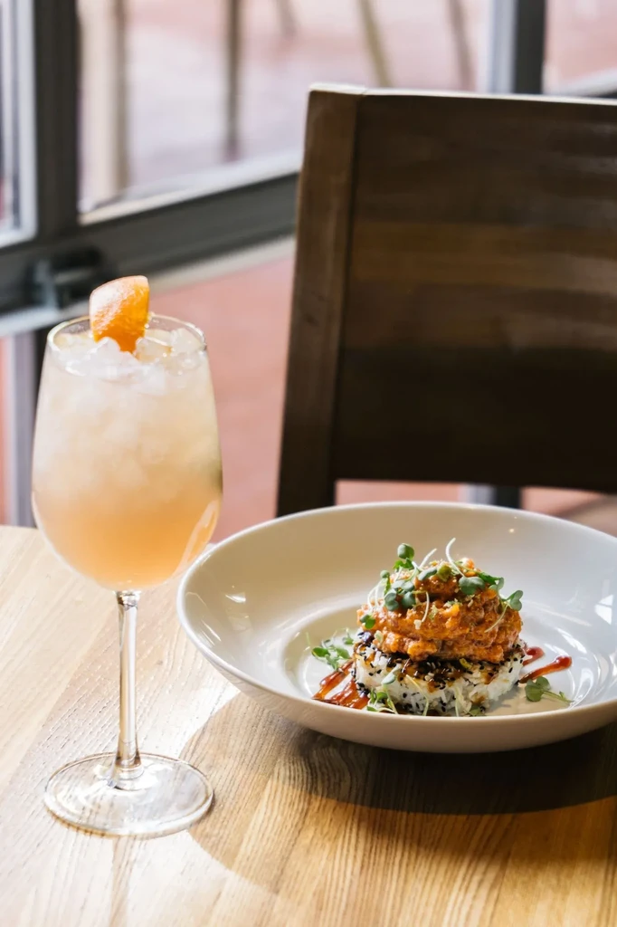 Orange cocktail and tartare rice bowl on a wooden table.