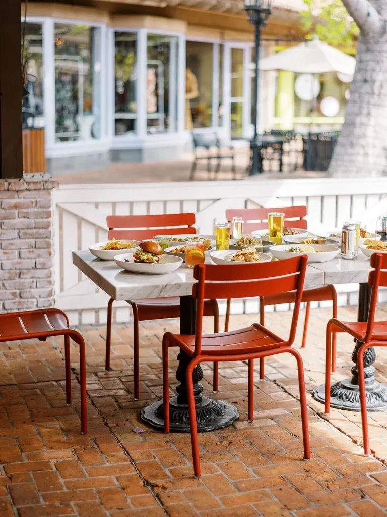 Outdoor marble table with pasta, salads, drinks, and rust-red chairs.