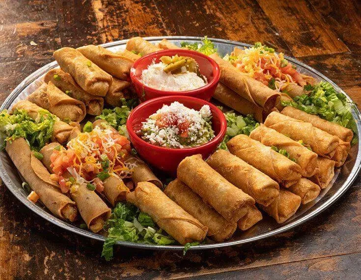 Platter of crispy taquitos with guacamole, creamy dip, cheese, and pico.