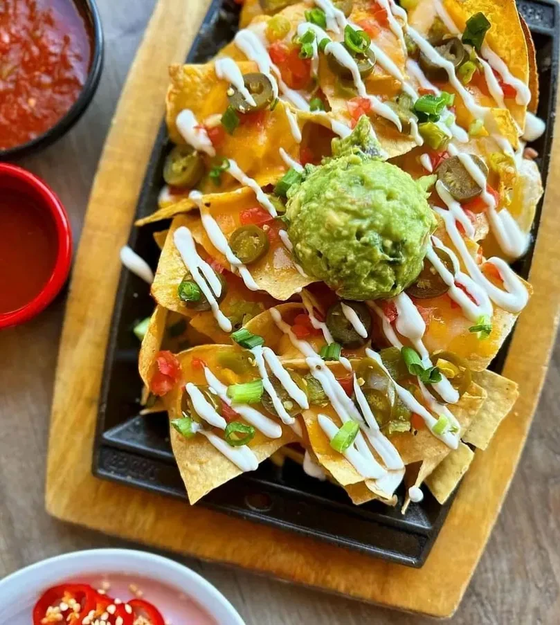 Nachos in cast-iron pan with cheese, guacamole, and jalapeños.