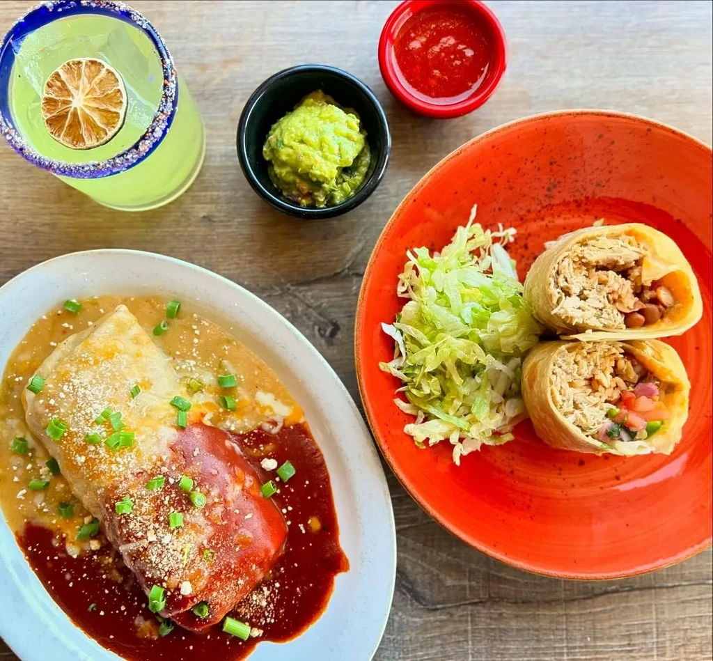 Top-down view of Mexican meal: sauced burrito, chicken burritos, guacamole, margarita.