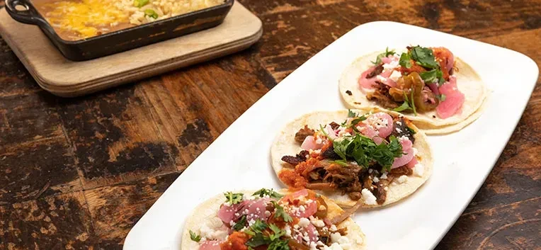 Three street tacos topped with salsa, cheese, cilantro; beans nearby.