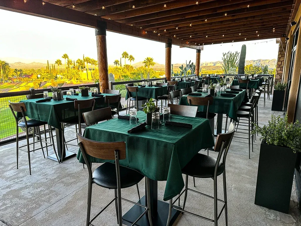 Outdoor patio with high-top green tables, desert golf course, mountains.