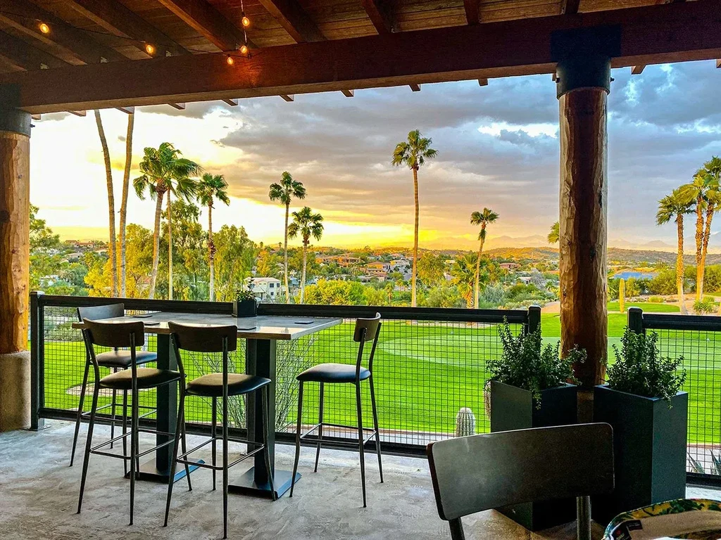 Outdoor restaurant patio with high-top tables overlooking a golf course at sunset.