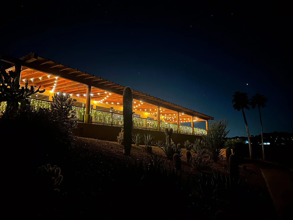 Single-story building with string-lit pergola, desert plants, and night sky.