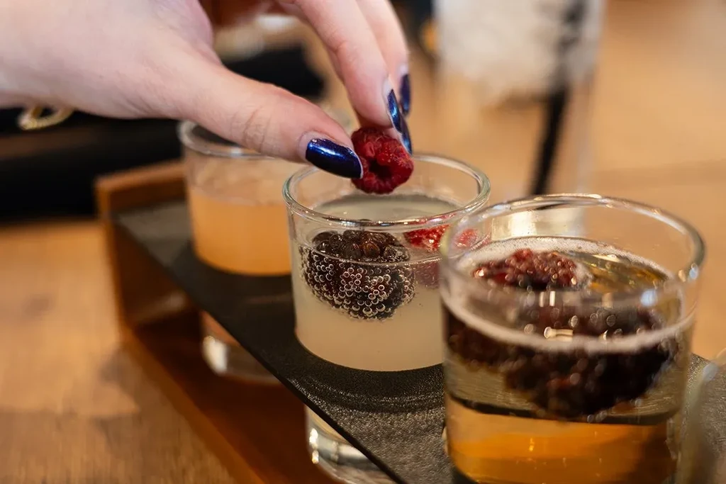 Hand drops raspberry into one of three glasses on a tray.