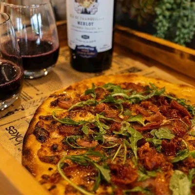 Gourmet pizza with sun-dried tomatoes, meat, arugula, and red wine.