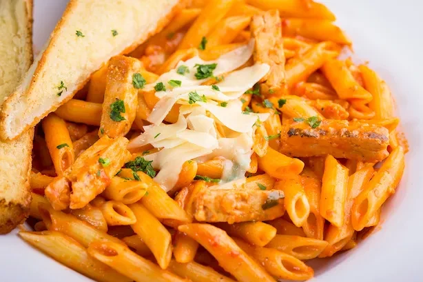 Penne pasta with chicken, red sauce, cheese, herbs, and toasted bread.