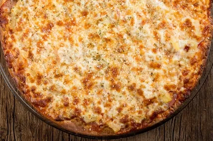 Close-up of a freshly baked Hawaiian pizza on a wooden table.