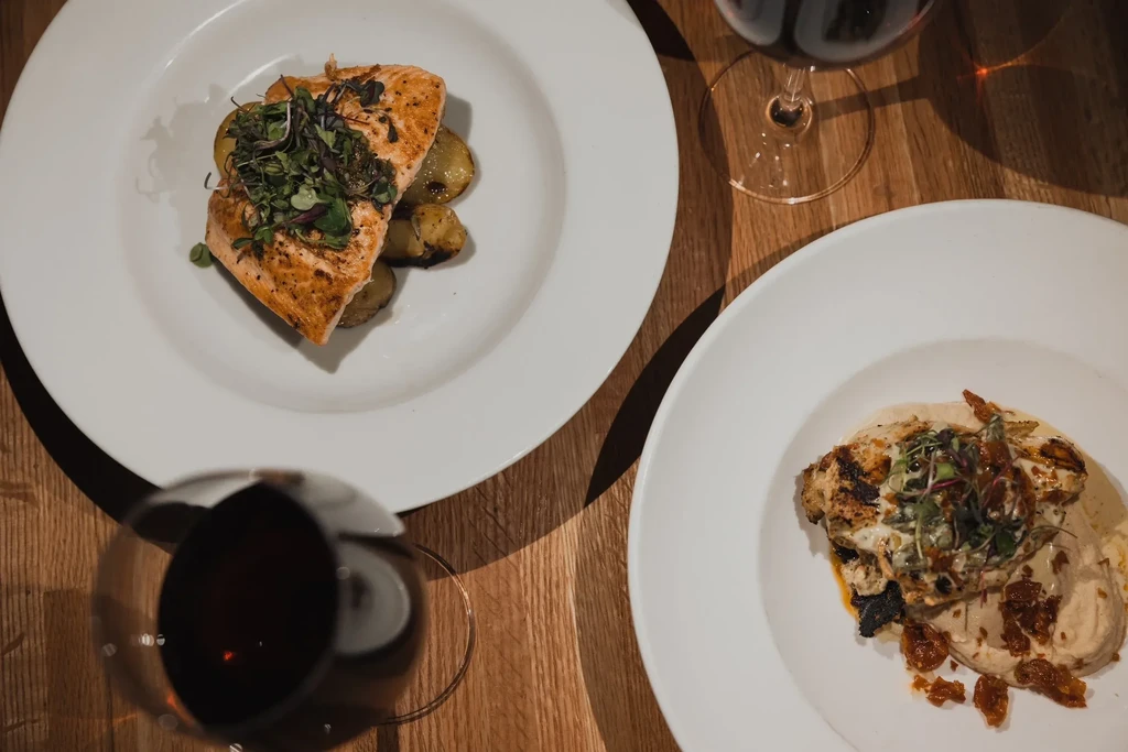Two plated restaurant dishes: salmon, another protein, and red wine.