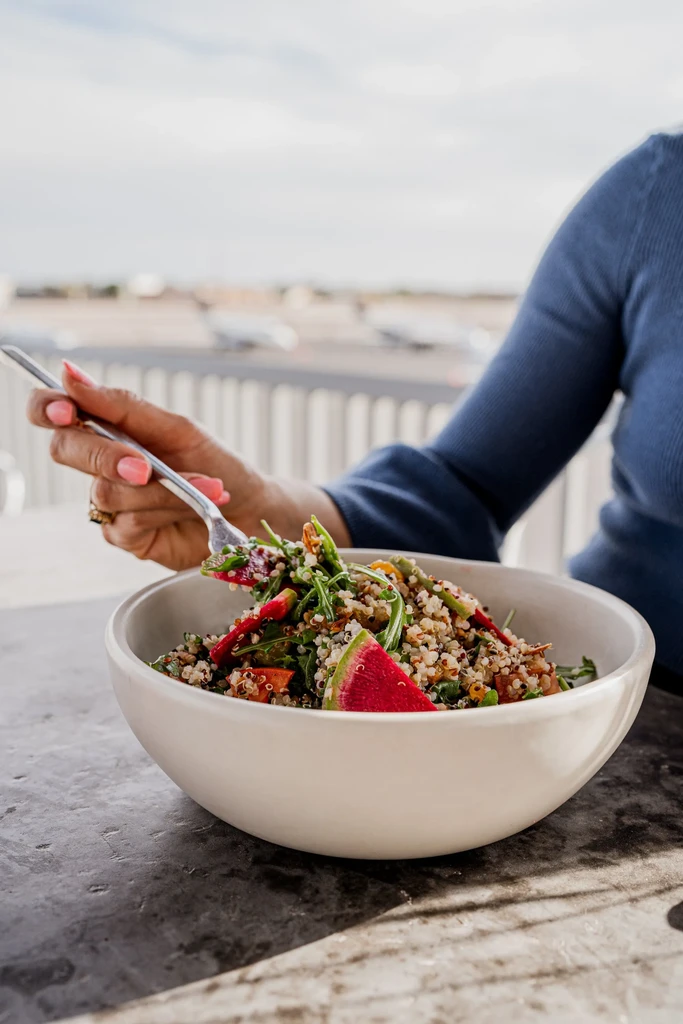 Hand with fork lifts colorful quinoa salad garnished with watermelon.