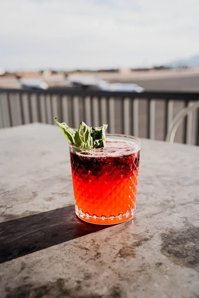 Two-tone cocktail with basil in faceted glass on outdoor table.