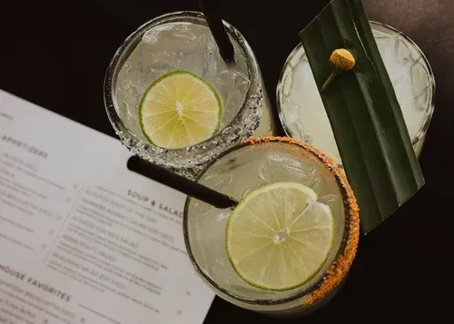 Overhead view of three garnished cocktails on a dark surface.
