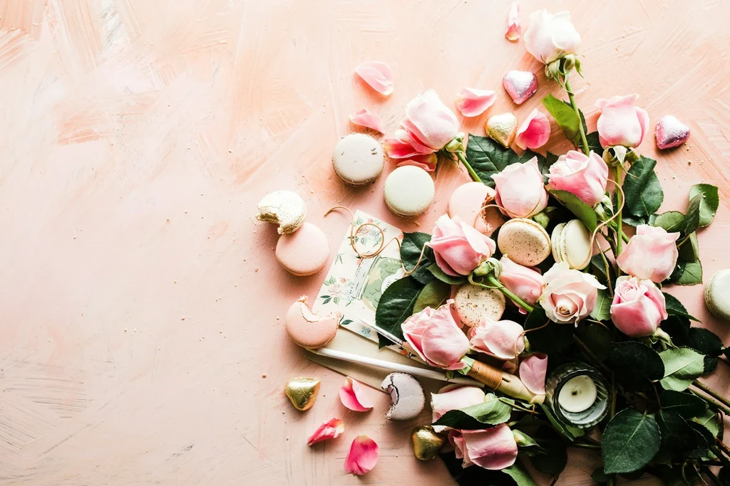 Flat lay: pink roses, pastel macarons, heart chocolates, decorative card.