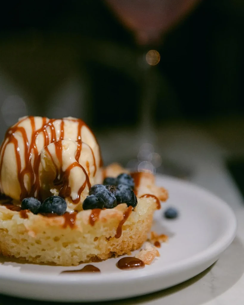 Waffle, vanilla ice cream, blueberries, and chocolate drizzle on a white plate.
