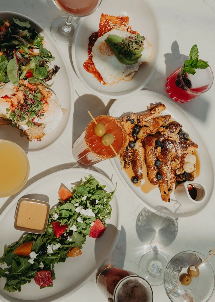 Overhead of a white table laden with diverse brunch food and drinks.