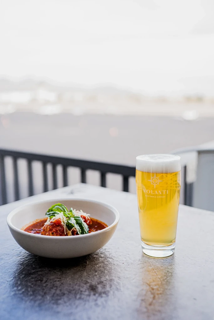Meatballs with basil, cheese, and beer on an outdoor table.