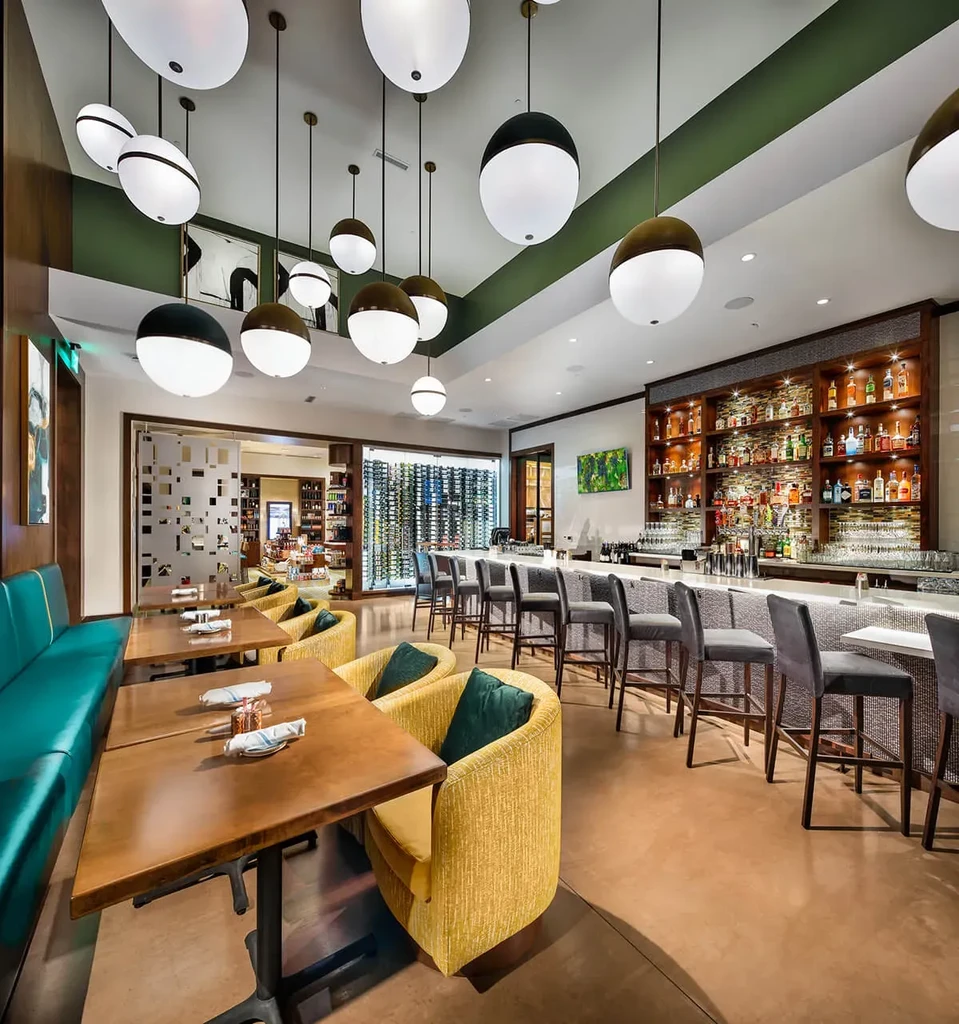 Modern restaurant and bar with teal banquettes, yellow chairs, and a wine cellar.