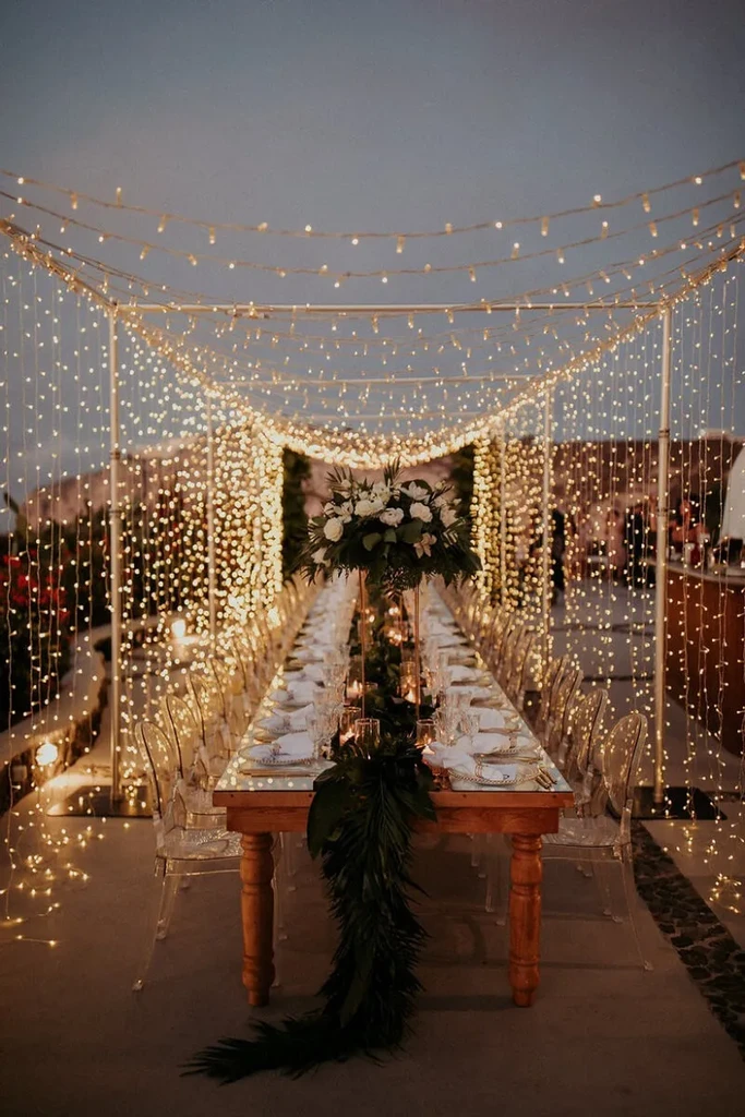 Elegantly set wooden dining table with foliage, candles, and string lights.
