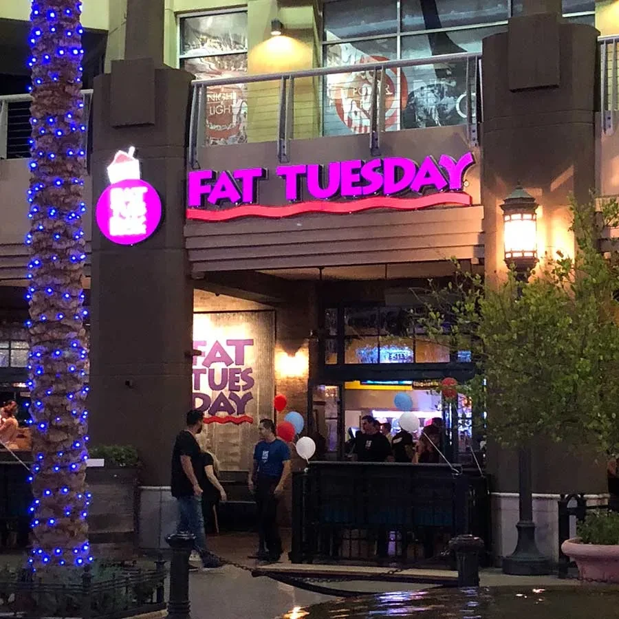 Fat Tuesday bar exterior at night with glowing magenta sign and lit palm.