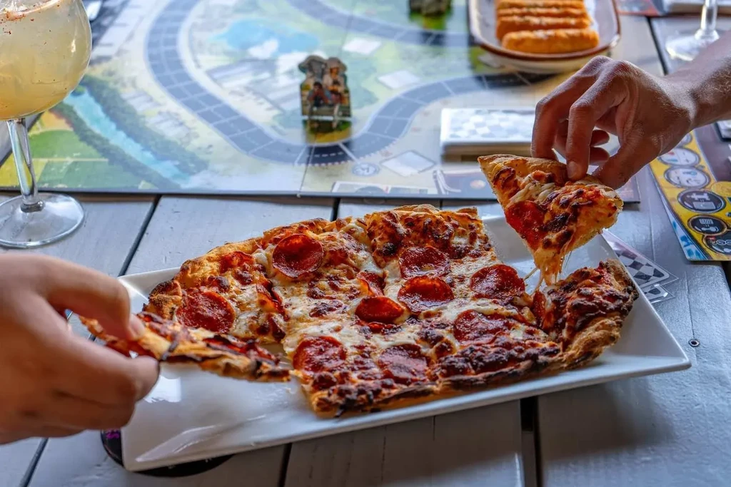 Square pepperoni pizza, hands pulling slices, stretching cheese, board game.
