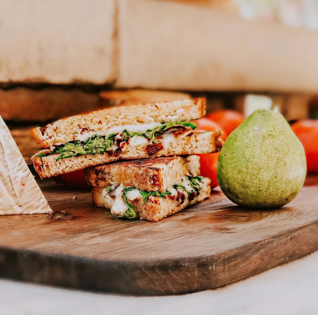 Grilled whole-grain sandwich, soft cheese, and pear on a rustic board.