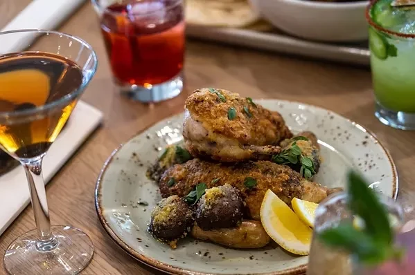 Crispy fried chicken, potatoes, lemon, herbs, and an amber cocktail on a table.