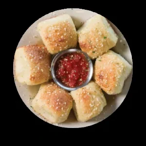 Close-up of six cheesy herb bread rolls around red dipping sauce.