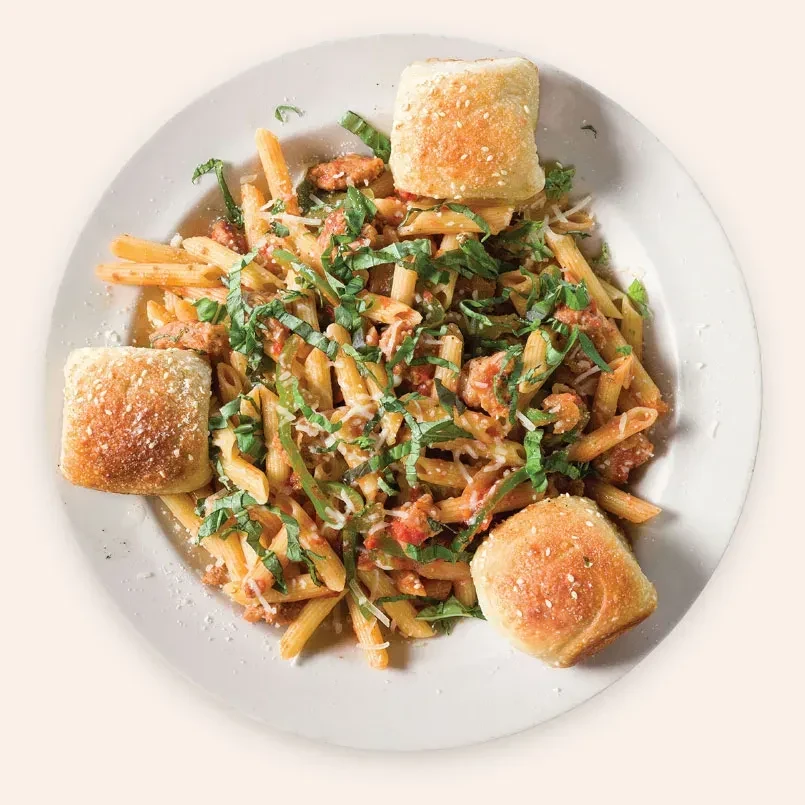 Penne pasta with meat sauce, basil, cheese, and three bread rolls.