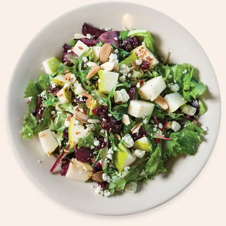 Fresh salad with greens, pear, cranberries, cheese, and almonds in a bowl.