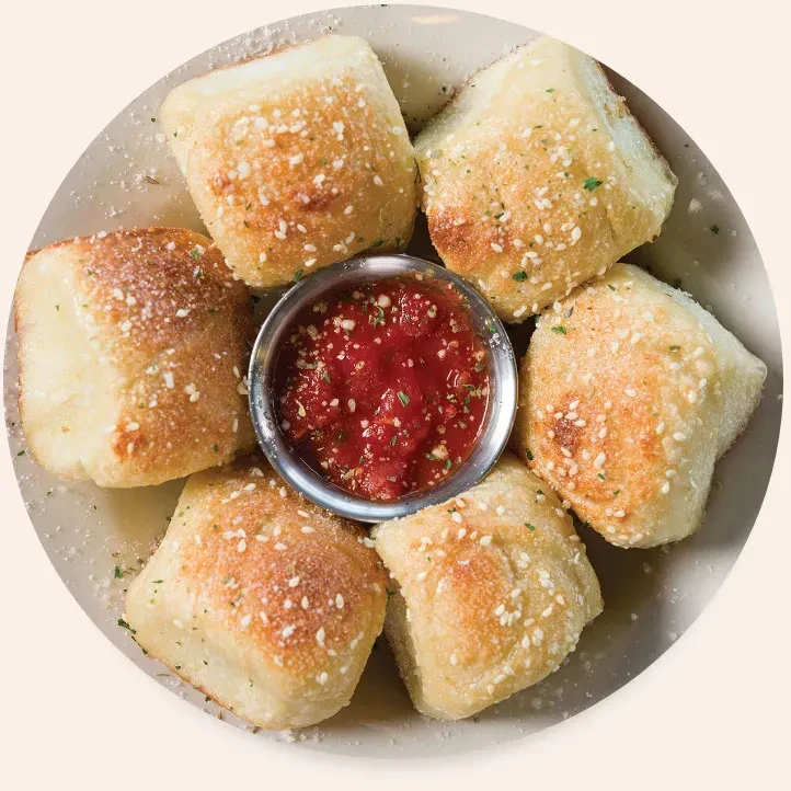 Six golden puffy bread bites with herbs and red marinara sauce.
