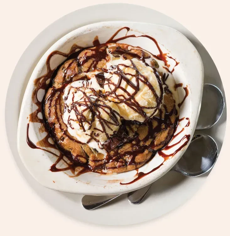 Top-down: Warm chocolate chip cookie, vanilla ice cream, chocolate syrup drizzled.