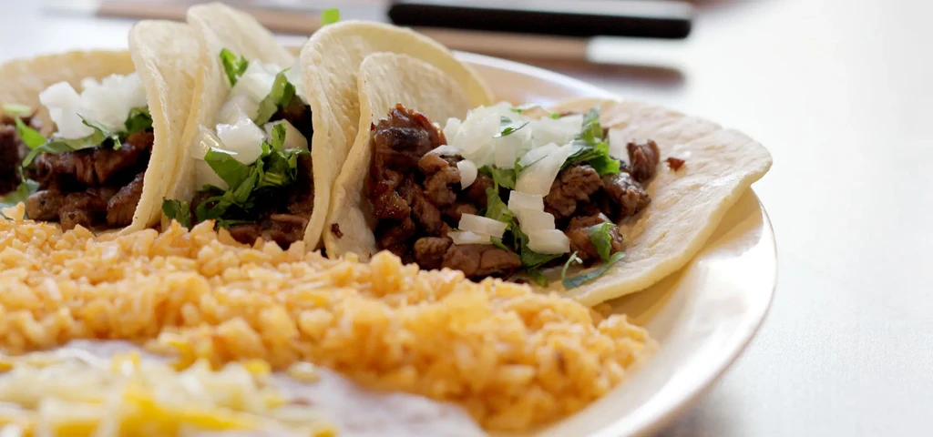Three street tacos with meat, onions, cilantro, served with Mexican rice.